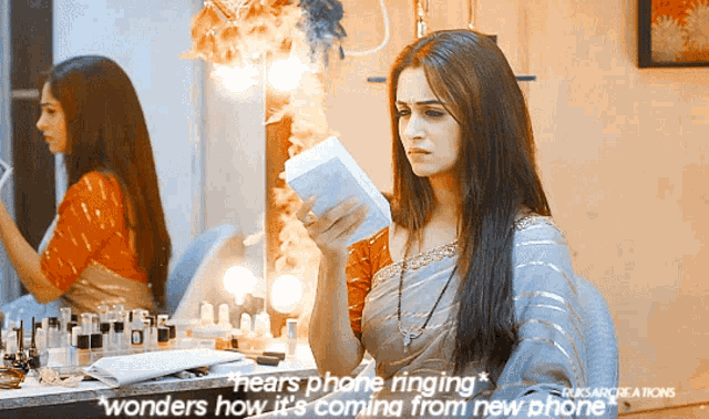 a woman sitting in front of a mirror holding a box that says ' hears phone ringing '