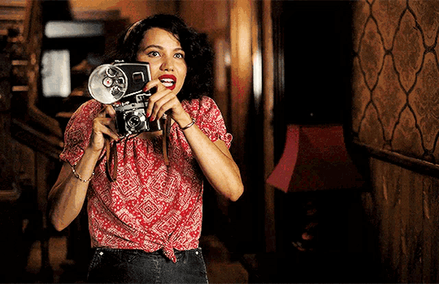 a woman in a red shirt is holding a camera with the letter l on the front