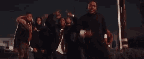 a group of men are standing next to each other on a street at night and dancing .