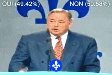 a man in a suit and tie is giving a speech in front of a sign that says oui 49.42% non 50.58%