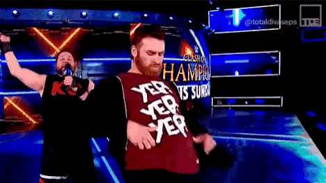 two wrestlers are standing on a stage and one of them is wearing a champion shirt .