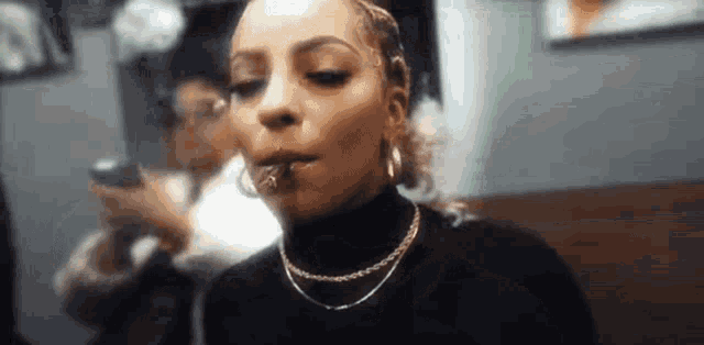 a woman is smoking a cigarette in a room with a phone in her hand .