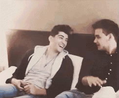 two young men are sitting on a couch and laughing