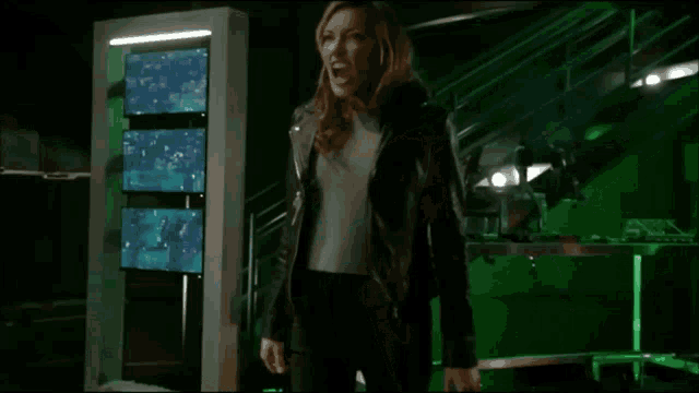 a woman in a black jacket is screaming in a green room