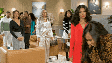 a group of women are standing in a living room with a portrait of a man on the wall