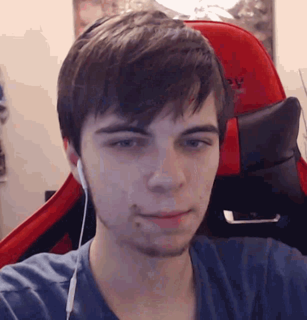 a young man wearing headphones looks at the camera while sitting in a red and black gaming chair