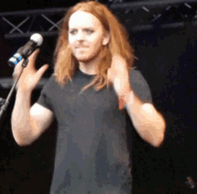 a man with long red hair is singing into a microphone on stage .