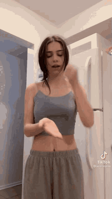 a woman in a crop top is standing in front of a white refrigerator .