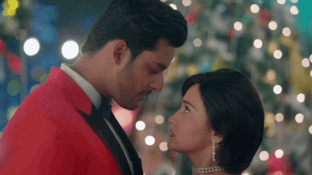a man and a woman are kissing in front of a christmas tree .