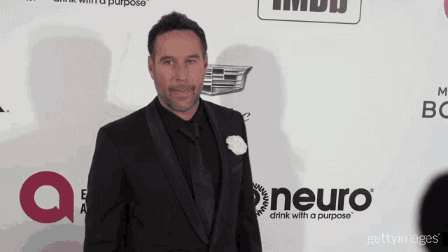 a man in a suit stands on a red carpet with a neuro logo