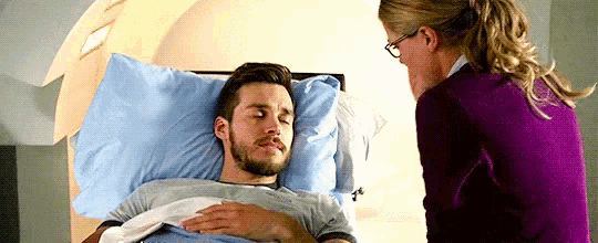 a man is laying in a hospital bed while a woman talks to him .