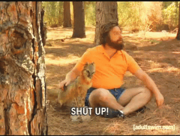 a man with a beard is sitting in the woods with a dog and says " shut up "