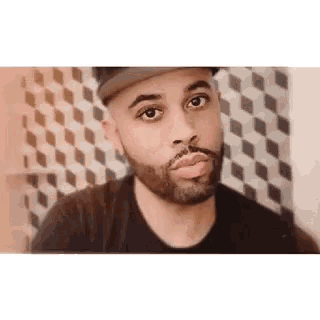 a man with a beard wearing a hat and a black shirt is making a funny face .