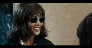 a woman wearing sunglasses and a wig smiles while talking to another woman .