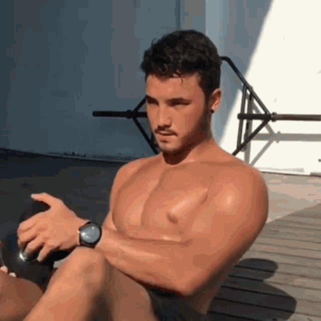 a shirtless man wearing a watch is sitting on a wooden deck .
