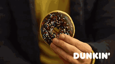a person holding a chocolate donut with sprinkles and dunkin ' on the bottom