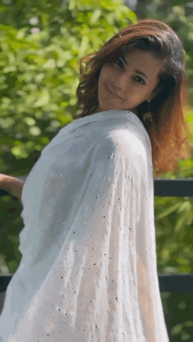 a woman wearing a white shawl is standing in front of trees