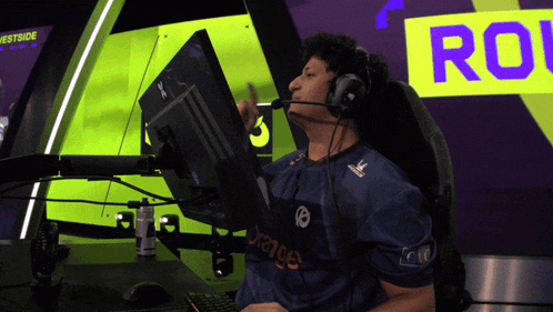 a man wearing headphones is sitting in front of a computer screen with orange on his shirt