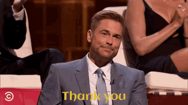 a man in a suit and tie is sitting in front of a screen that says thank you