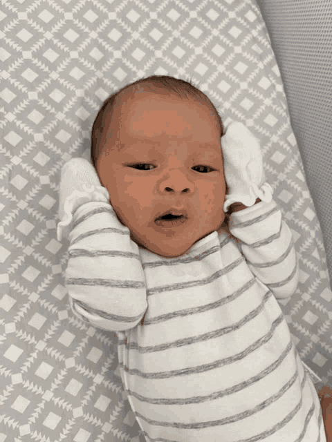 a baby in a striped shirt is laying on a gray and white blanket