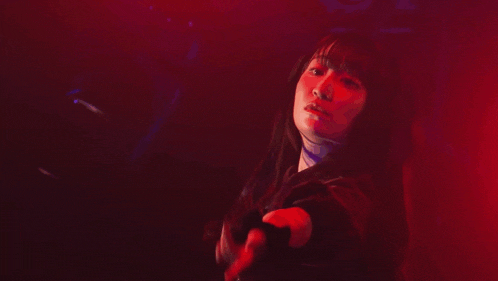 a woman is standing in a dark room with a red light behind her