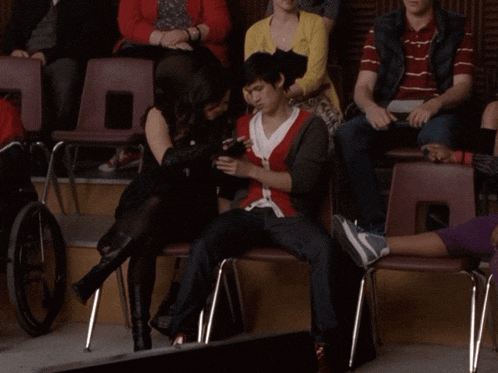 a group of people sitting in chairs including a man in a red cardigan