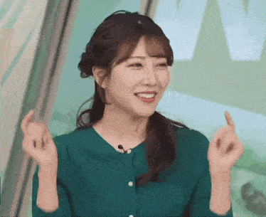 a woman in a green shirt is smiling and making a heart shape with her hands