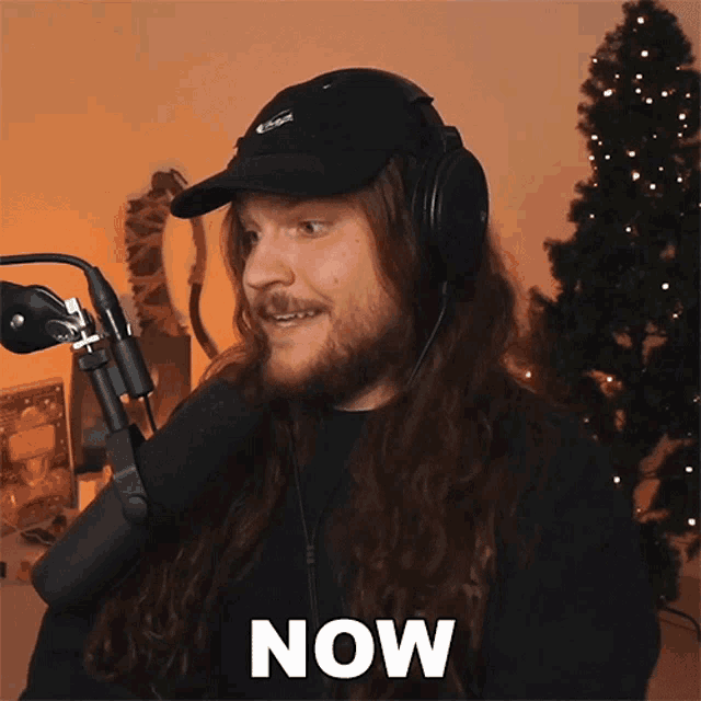 a man wearing headphones and a black hat says now