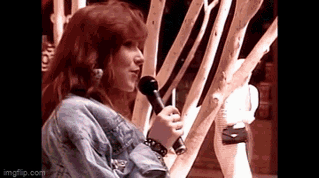 a woman in a denim jacket is holding a microphone in her hand .