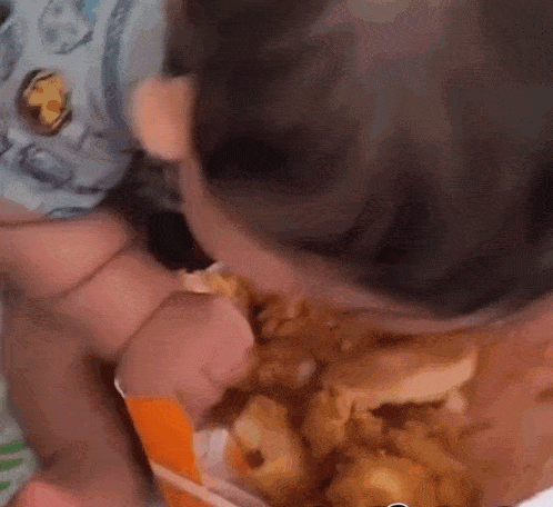 a baby is eating fried chicken from a container .