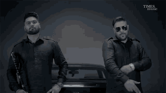 two men standing next to each other with times music written on the bottom right