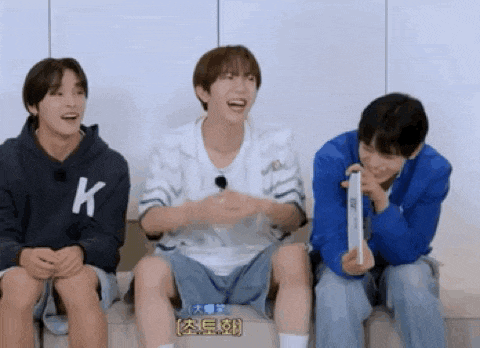 three young men are sitting next to each other on a couch . one of the men is wearing a k hoodie .