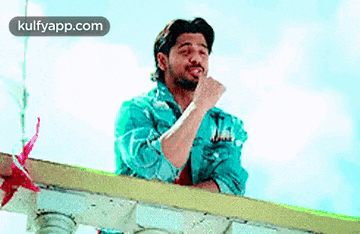 a man in a blue shirt is standing on a balcony and making a funny face .