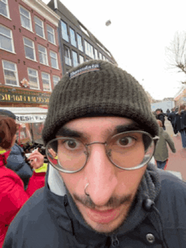 a man wearing glasses and a beanie stands in front of a sign that says fresh