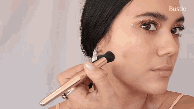 a woman is applying makeup with a brush and the word bustle is on the bottom right