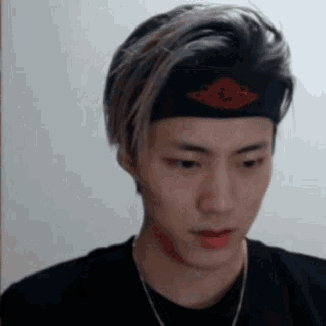 a young man wearing a headband and a necklace looks at the camera .