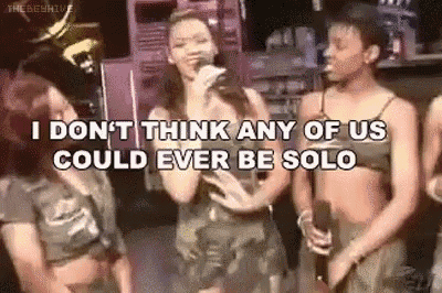 a group of women are standing next to each other in a room and a woman is singing into a microphone .