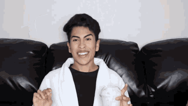 a young man wearing a white robe is sitting on a black couch