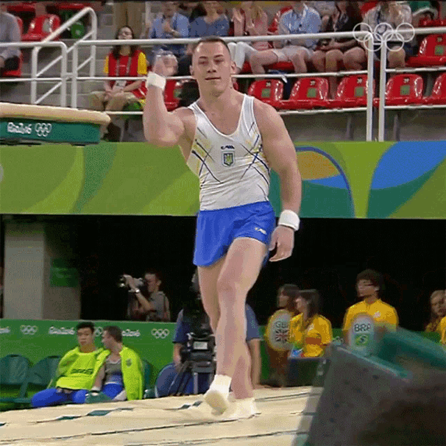 a man in a white tank top and blue shorts is doing a trick in front of a crowd at the rio 2016 olympics