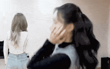 two women are standing next to each other and one is covering her face