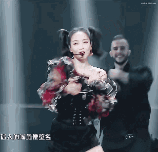 a woman with pigtails is dancing in front of a man with chinese writing on the bottom right