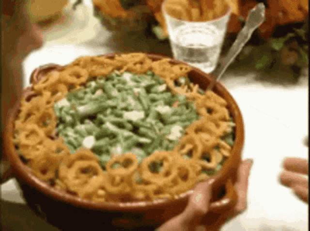 a person is holding a bowl of food with green beans and onion rings