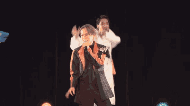 a man singing into a microphone while another man dances behind him