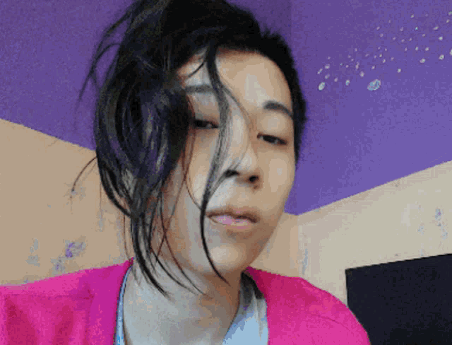 a woman in a pink sweater looks at the camera with a purple wall in the background