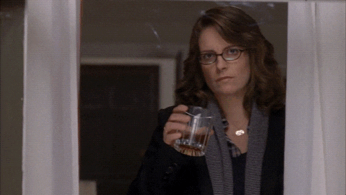 a woman holding a glass of whiskey looks out a window