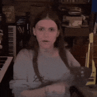 a young woman with long hair is sitting in front of a piano and a guitar .