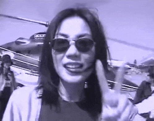 a woman wearing sunglasses is giving a peace sign in front of a helicopter