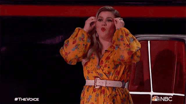 a woman in a yellow floral dress is giving a speech on nbc 's the voice show
