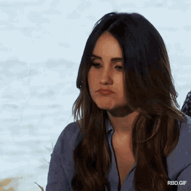 a woman with long hair is making a funny face while sitting in front of the water .