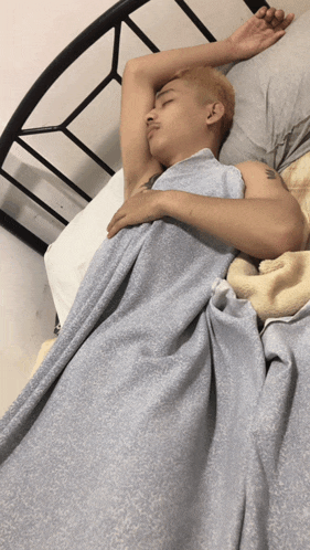 a man with a tattoo on his arm is sleeping on a bed with a blue blanket
